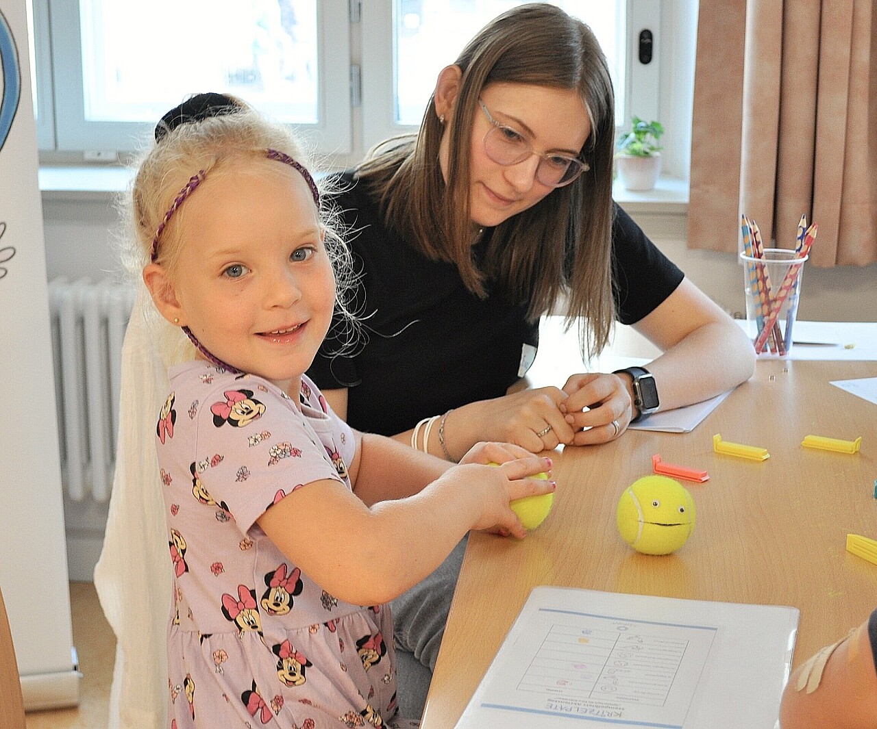 Kind und Kritzelpatin führen gemeinsam eine Übung mit einem Tennisball durch